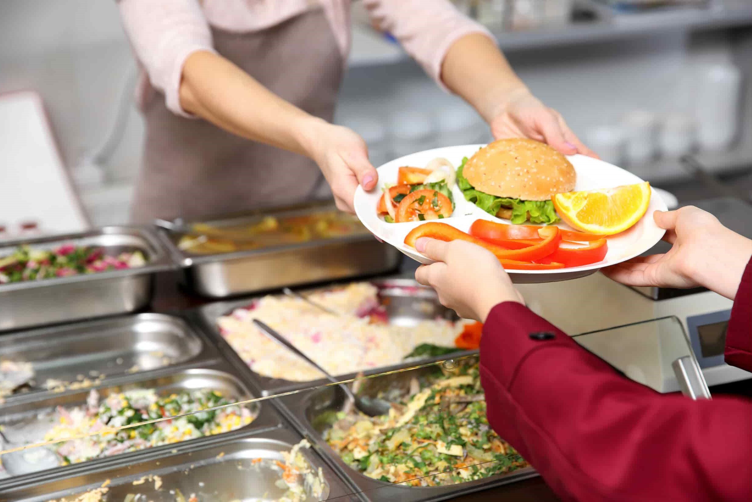 personal de servicio sirve una bandeja de alimentos a un colaborador en el comedor de la empresa